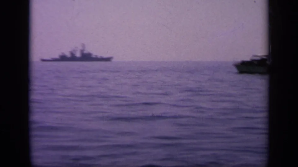 1963 Greece 8mm frame with a distant naval warship silhouette across calm water under a hazy sky.