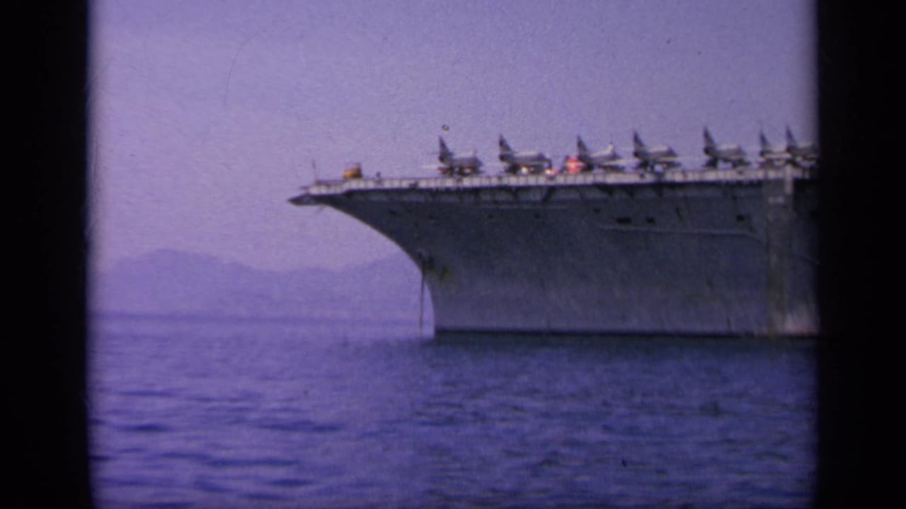 1963 Greece 8mm frame showing the bow of an aircraft carrier with multiple aircraft lined along the deck.