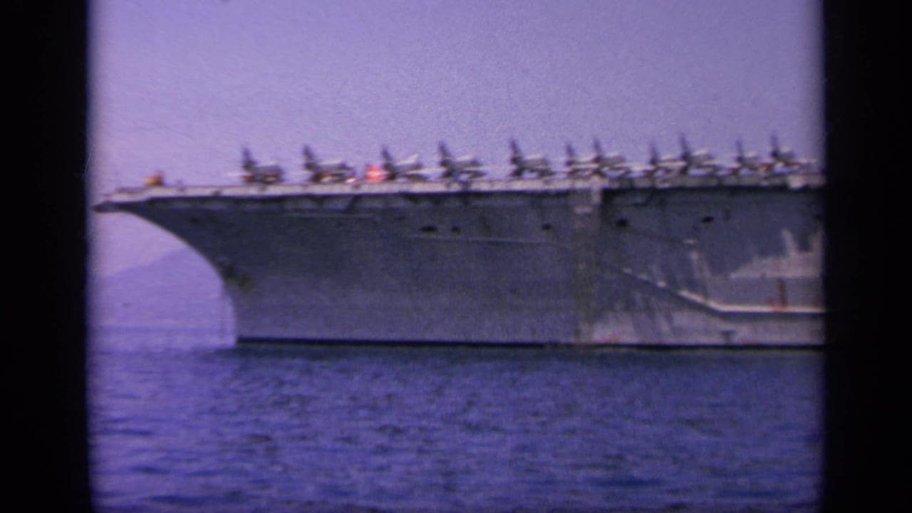 1963 8mm view near Greece of a U.S. Navy aircraft carrier broadside at sea, with fighter jets parked along the flight deck.