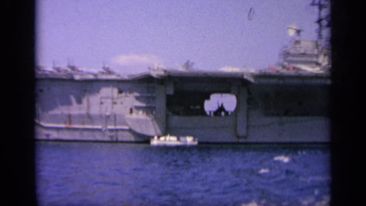 Midsection of an aircraft carrier with a small boat alongside on the water.