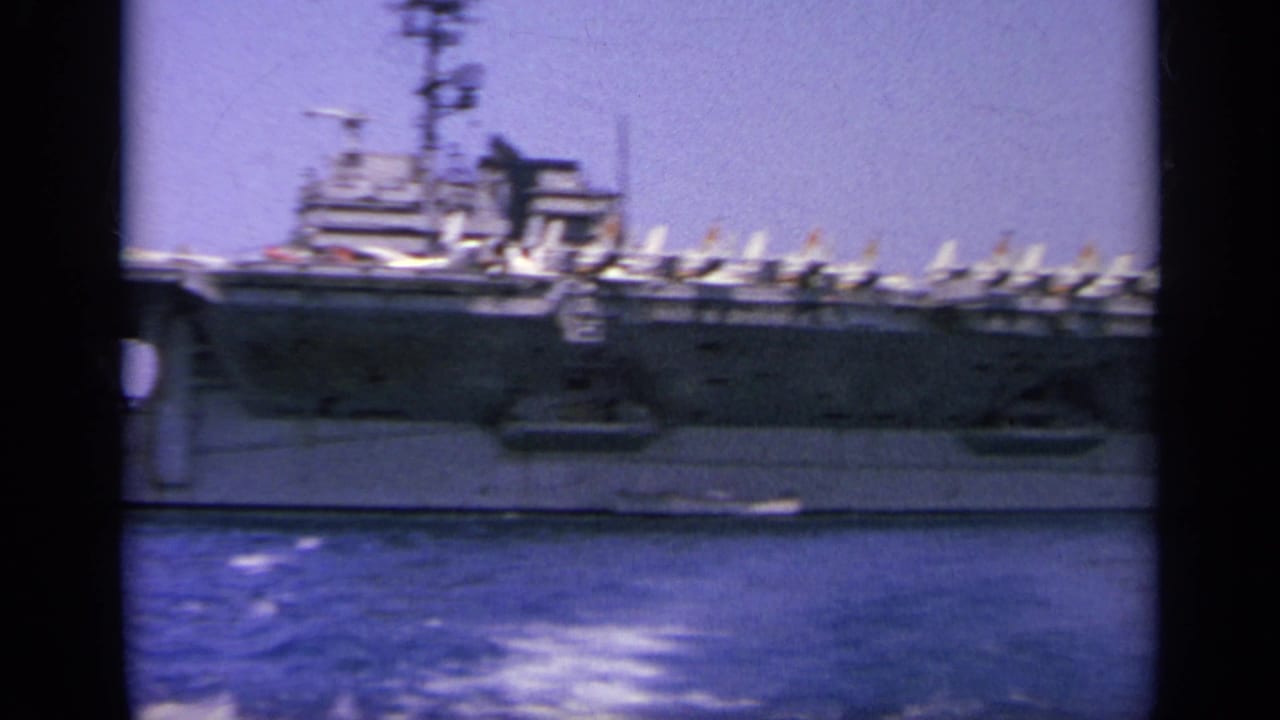 Handheld 1963 8mm view of the carrier island and flight deck, with rows of jets visible against the sky and water.