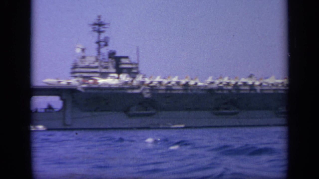 1963 Greece 8mm frame showing the carrier broadside, with its island structure, deck aircraft, and blue water in the foreground.
