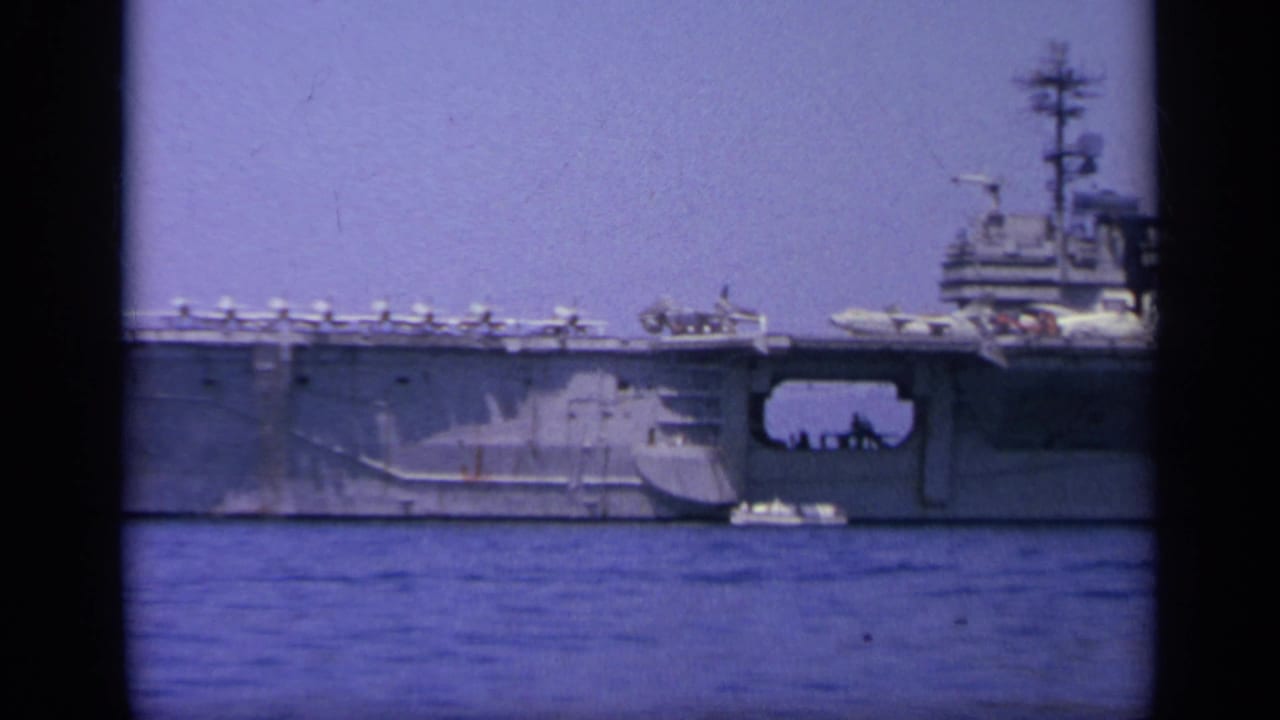 1963 Greece 8mm frame showing the carrier midsection and island area, with rows of aircraft on deck and water in the foreground.