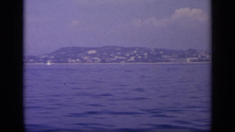 1963 Greece 8mm view from a boat toward a distant coastal hillside city across calm blue water.