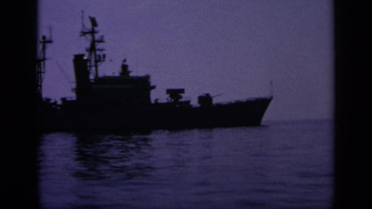 A silhouetted naval ship appears on calm water in 1963 Greece footage, with rigging and superstructure visible against the sky.