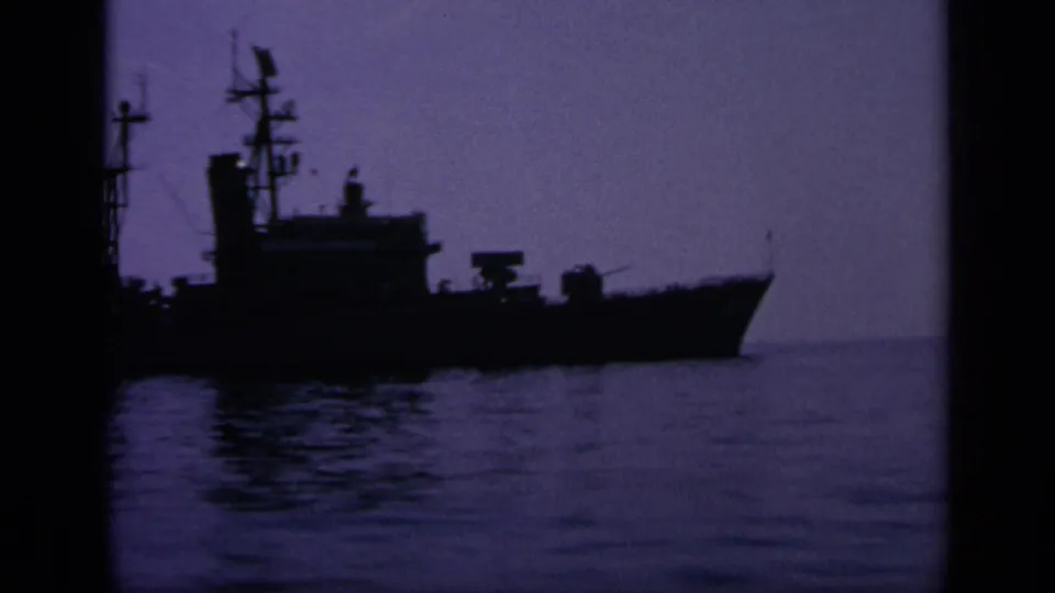 A silhouetted naval ship appears on calm water in 1963 Greece footage, with rigging and superstructure visible against the sky.