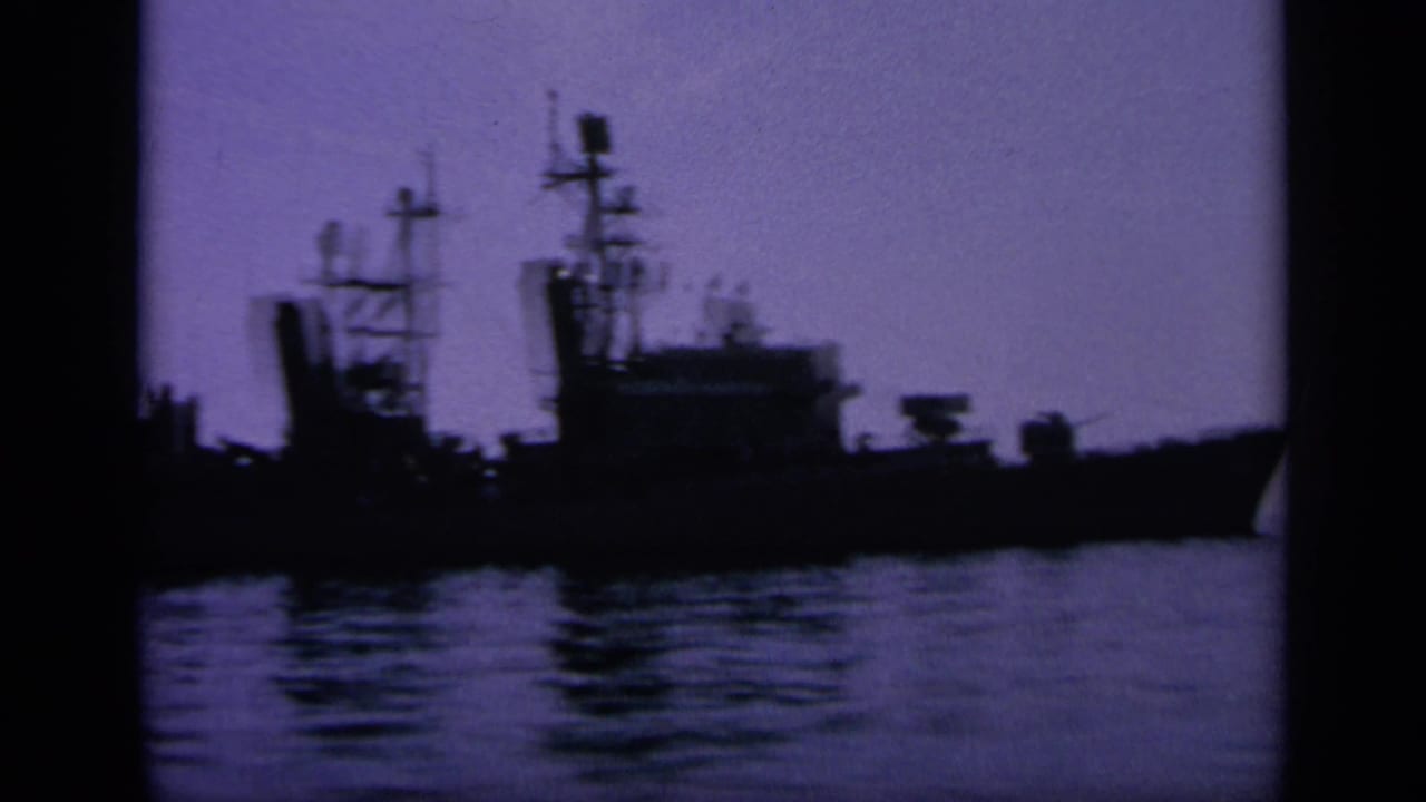 1963 Greece 8mm frame showing distant naval vessels silhouetted in harbor at dusk, with masts and water reflections visible.