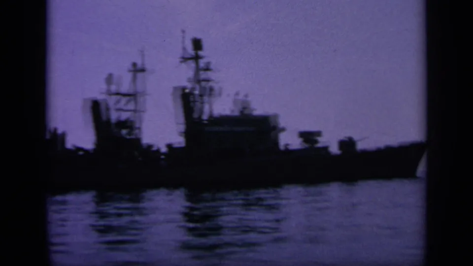 1963 Greece 8mm frame showing distant naval vessels silhouetted in harbor at dusk, with masts and water reflections visible.