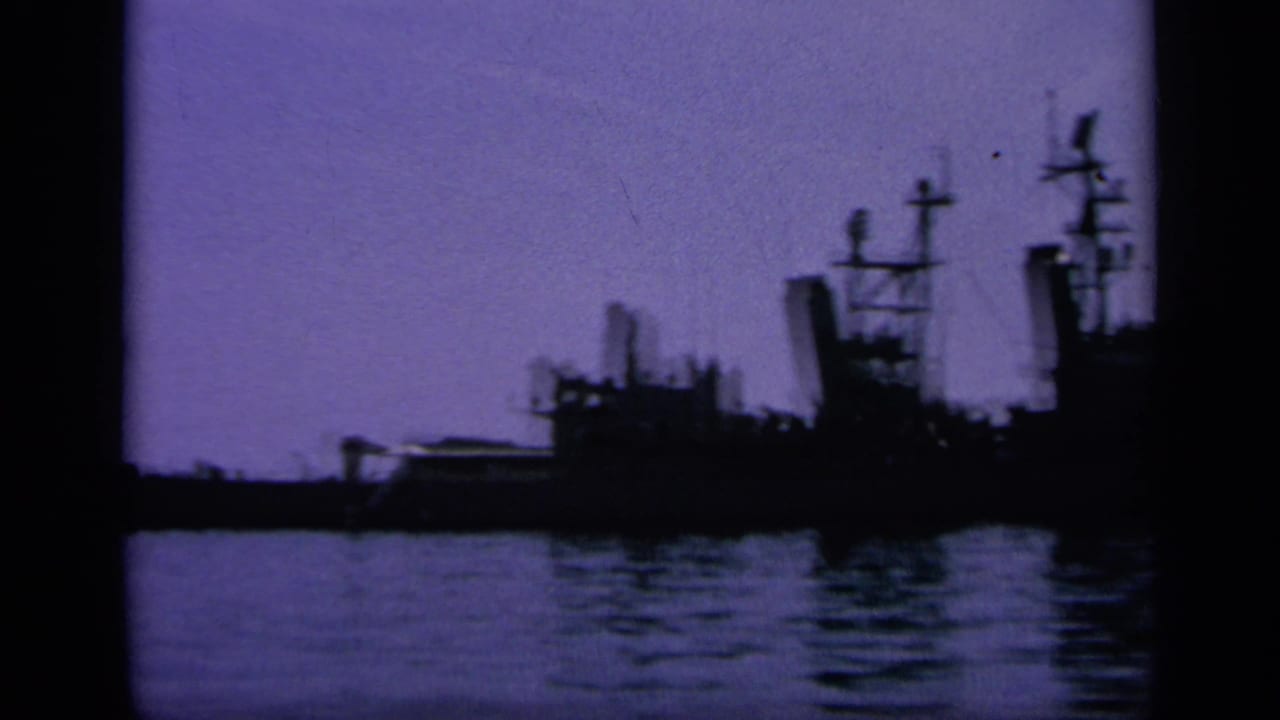 Distant naval ship shapes in a Greek harbor, filmed on 8mm with a purple twilight cast and soft low-light detail.