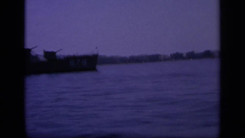 1963 Greece 8mm frame showing a dim naval vessel marked 878 crossing calm bay water with a low shoreline behind it.