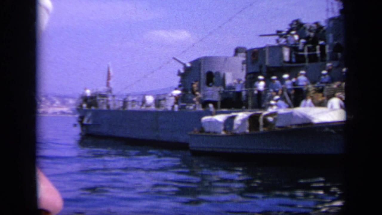1963 Greece 8mm frame showing a naval vessel at sea, crew on deck, a small boat alongside, and distant coast.