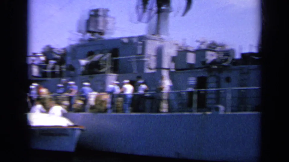 1963 Greece 8mm view of sailors standing along a gray naval ship, with deck equipment and railings visible.