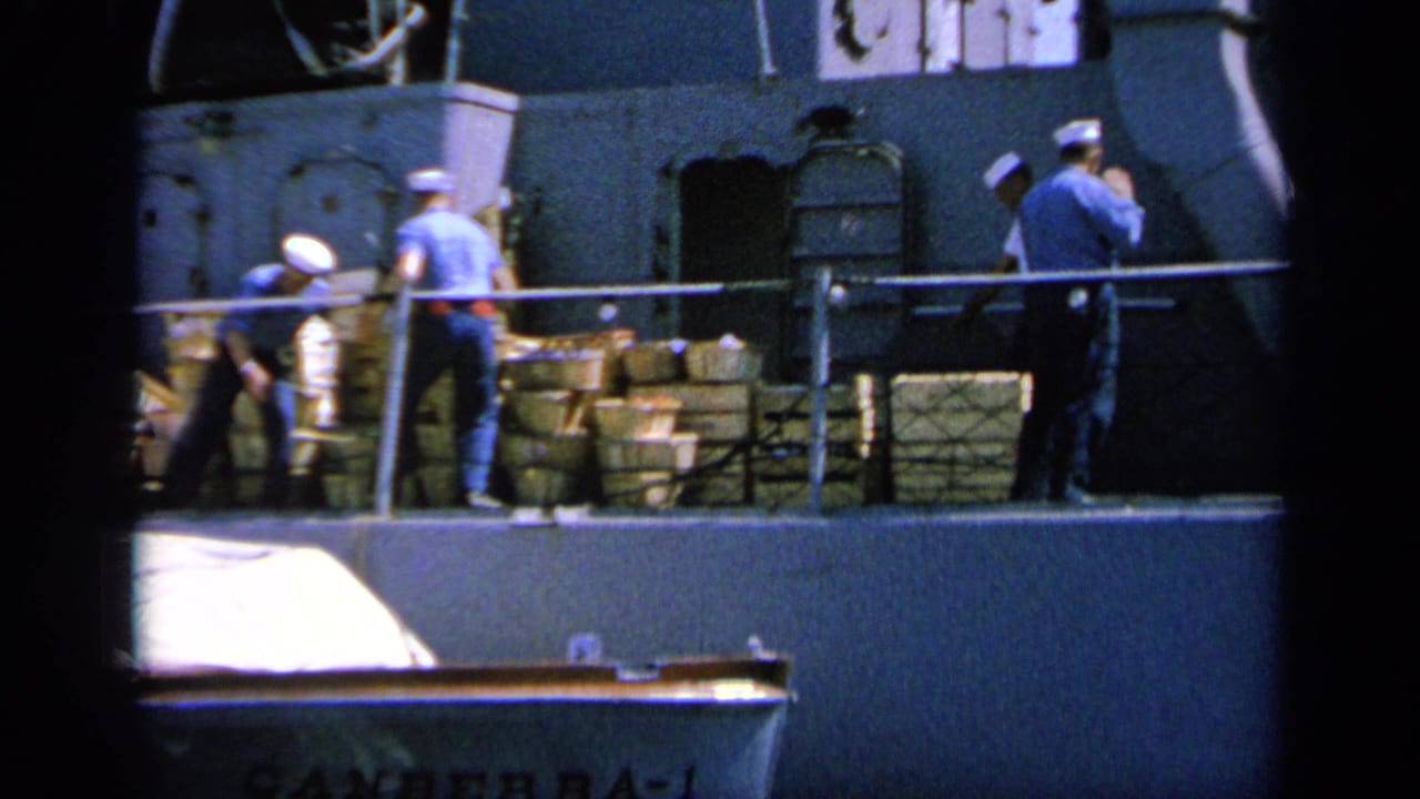 1963 Greece 8mm frame showing sailors on a naval deck with stacked supplies, railings, and a small boat below.