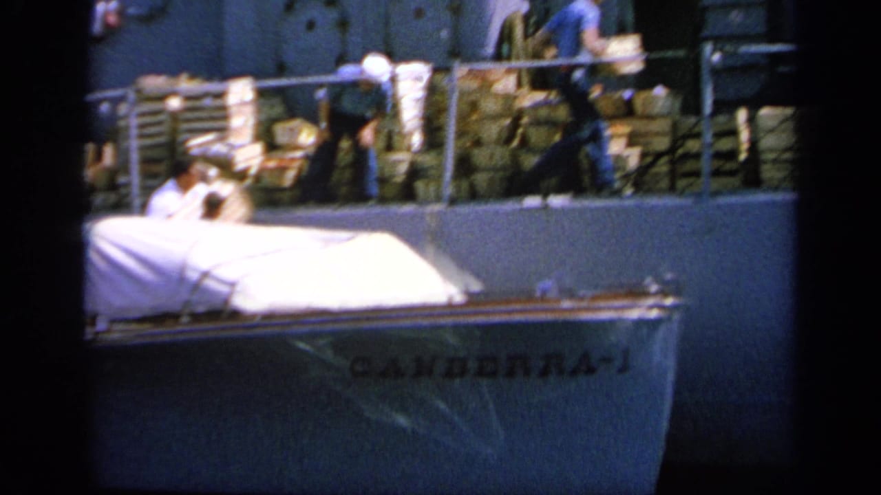 1963 Greece 8mm frame showing sailors near stacked supplies and covered equipment on a naval ship deck.