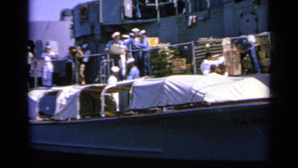 1963 Greece 8mm frame with sailors in blue and white uniforms gathered by supplies on a naval ship deck.