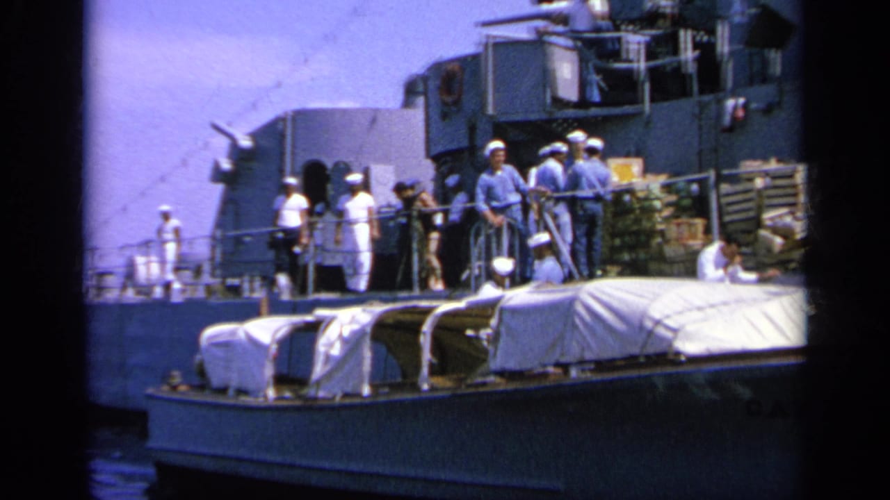 1963 Greece 8mm frame showing sailors and possible civilians on a naval deck with crates and canvas-covered gear.