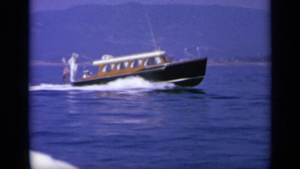 1963 Greece 8mm frame showing a small motorboat moving across open water near a distant shoreline.