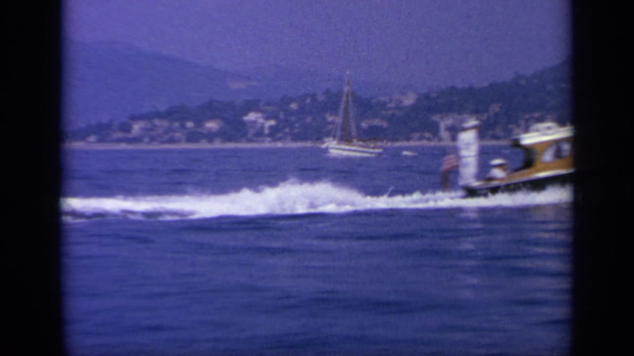 1963 Greece home-movie view of the speedboat exiting the frame while its wake spreads across the blue coastal water.