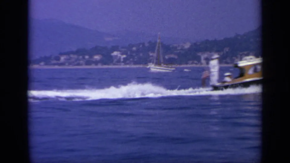 1963 Greece home-movie view of the speedboat exiting the frame while its wake spreads across the blue coastal water.