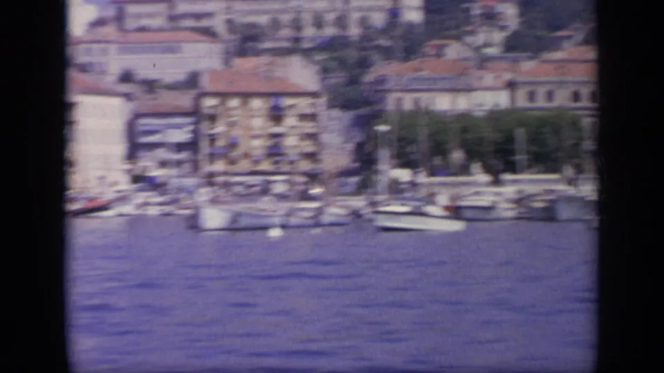 1963 Greece harbor view with small boats, masts, blue water, and waterfront town buildings along the port.