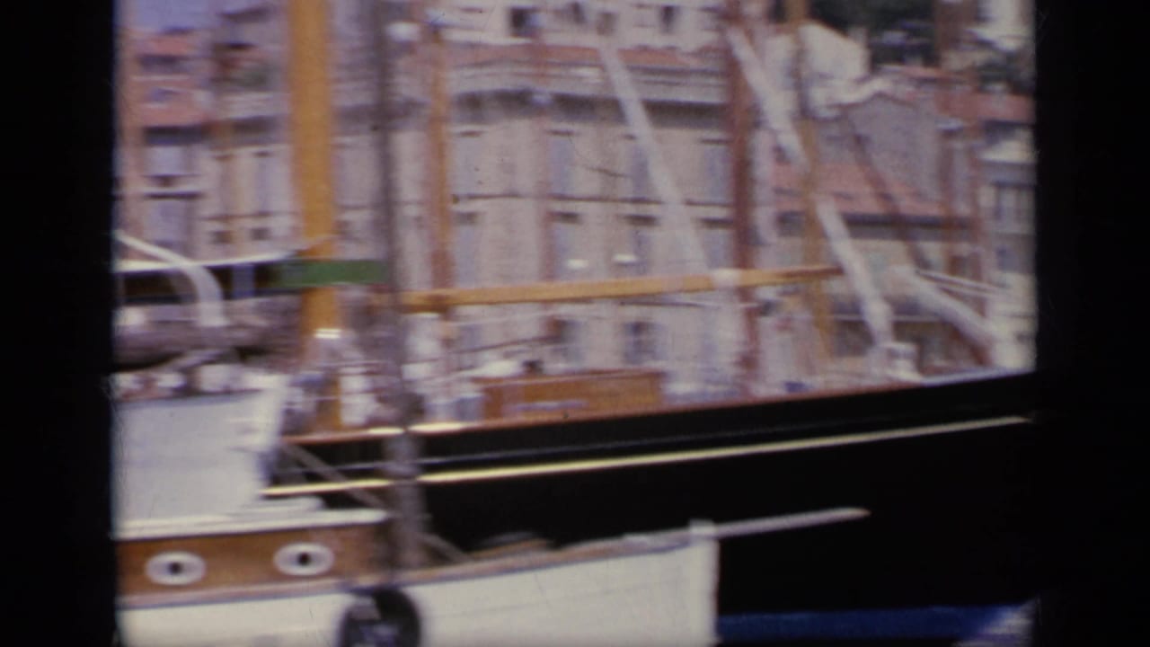 Wooden boats and masts beside a harbor quay with buildings in the background.