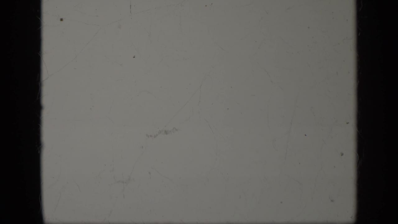 A mostly blank 8mm frame with pale exposure, dust, scratches, and dark gate edges from the same 1963 Greece home-movie clip.
