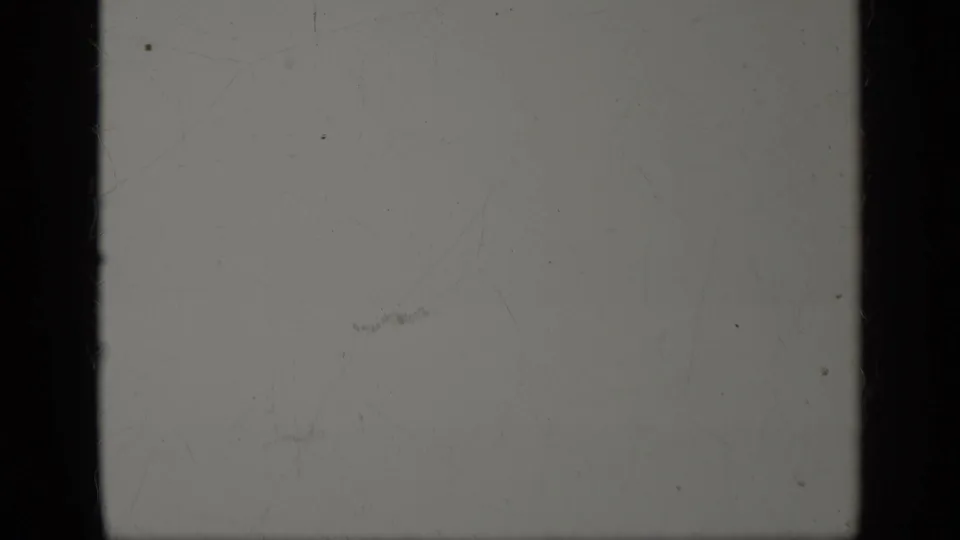 A mostly blank 8mm frame with pale exposure, dust, scratches, and dark gate edges from the same 1963 Greece home-movie clip.