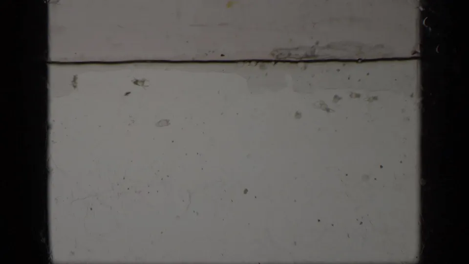 End frame from the 1963 Greece 8mm clip showing blank leader-like film, scratches, dust, a horizontal line, and dark gate borders.