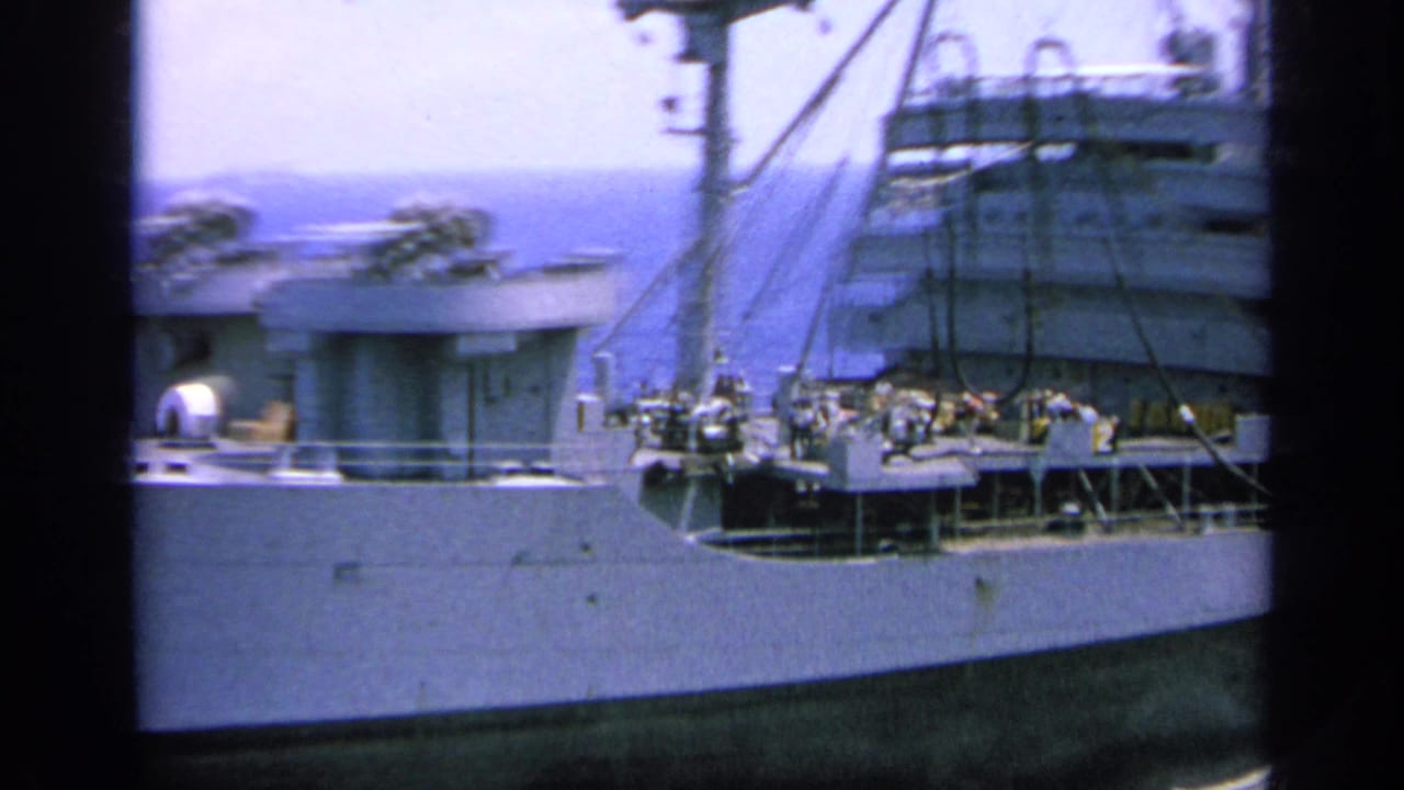 8mm frame showing the ship's side, deck railings, rigging lines, and upper structures during a close pass at sea.
