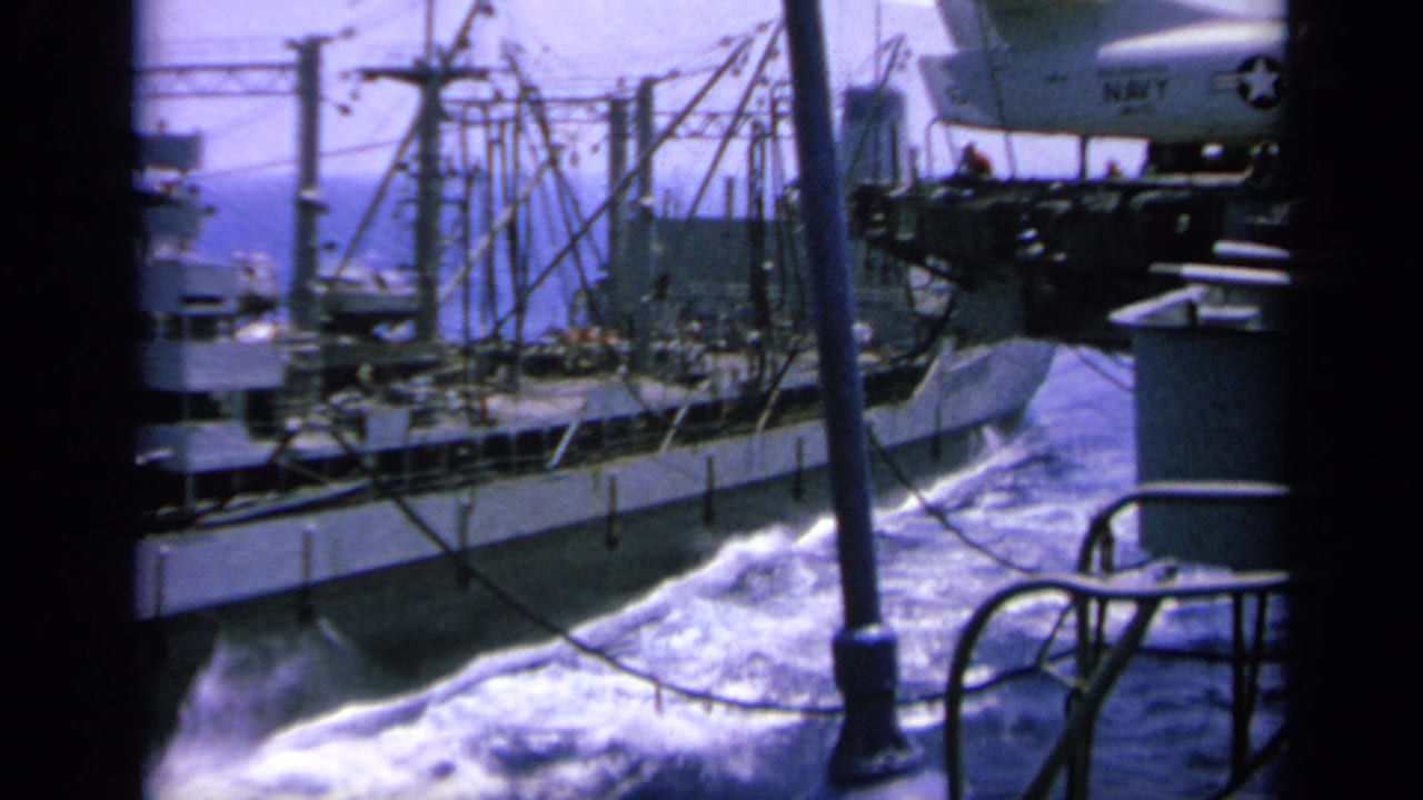 1963 Greece 8mm frame with ship rigging, white wake, carrier deck railings, and part of a parked naval aircraft.