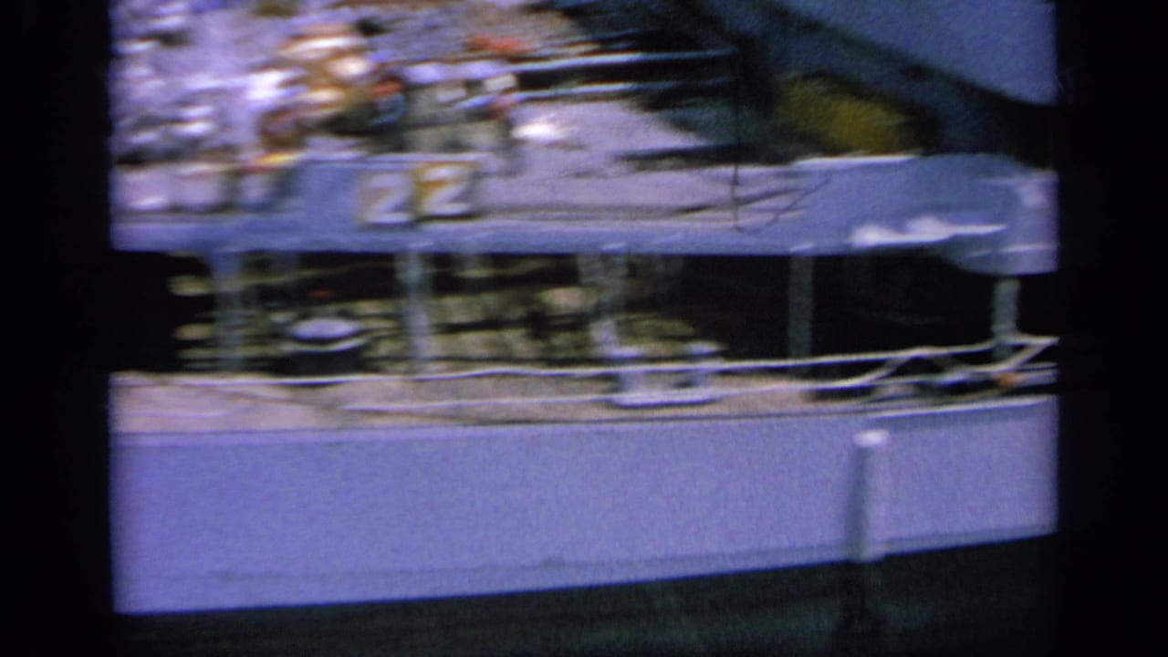 Blue-cast 8mm frame of the naval ship deck at port, showing railings, fittings and indistinct deck activity.