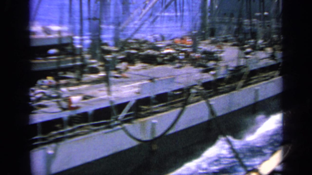 1963 Greece 8mm frame showing a large vessel's side, deck gear and white wake as it moves through blue water.