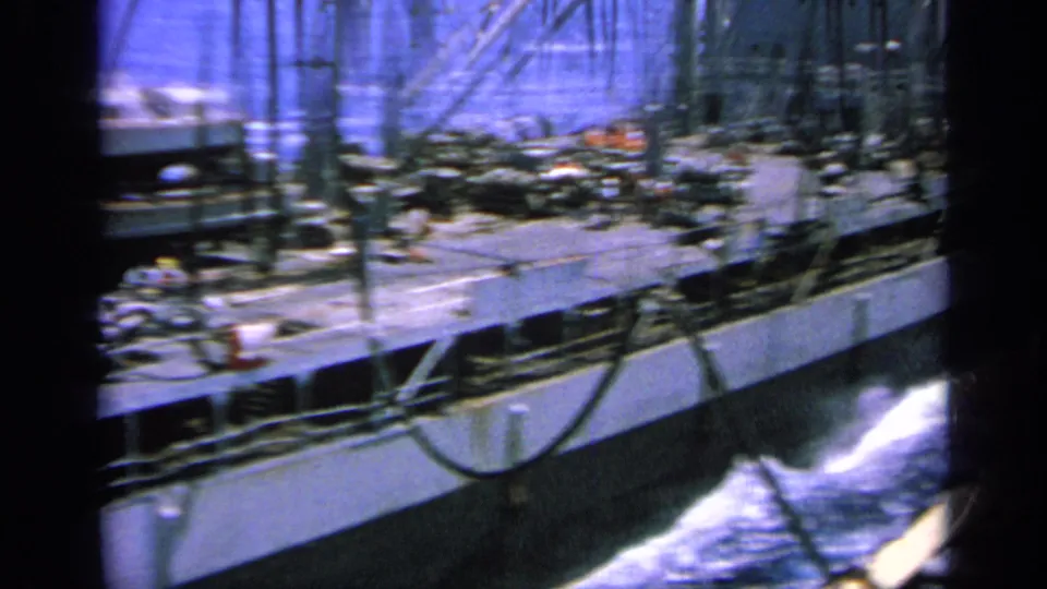 1963 Greece 8mm frame showing a large vessel's side, deck gear and white wake as it moves through blue water.