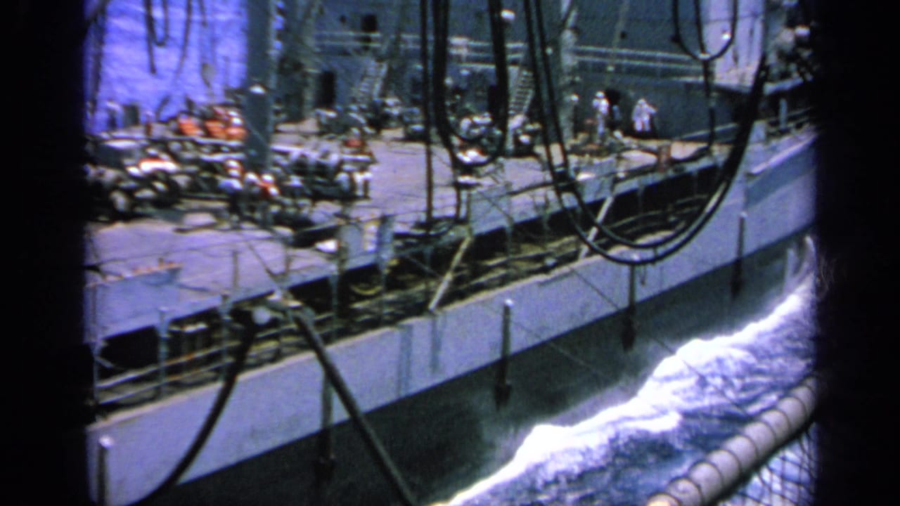 1963 Greece 8mm view of crew figures on a large ship deck, with hanging cables and white wake alongside.