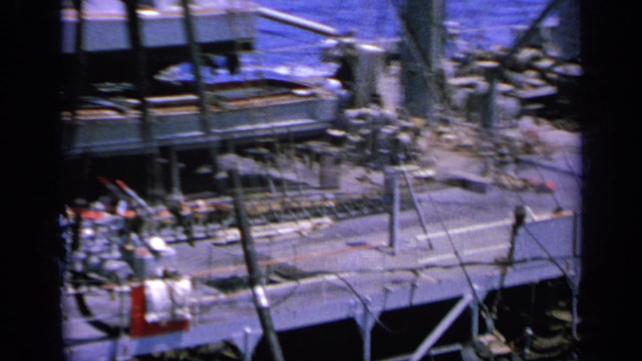 1963 Greece home-movie frame of an upper ship deck with metal railings, stairs, rigging, and deck equipment near the sea.