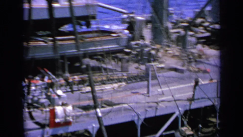 1963 Greece home-movie frame of an upper ship deck with metal railings, stairs, rigging, and deck equipment near the sea.