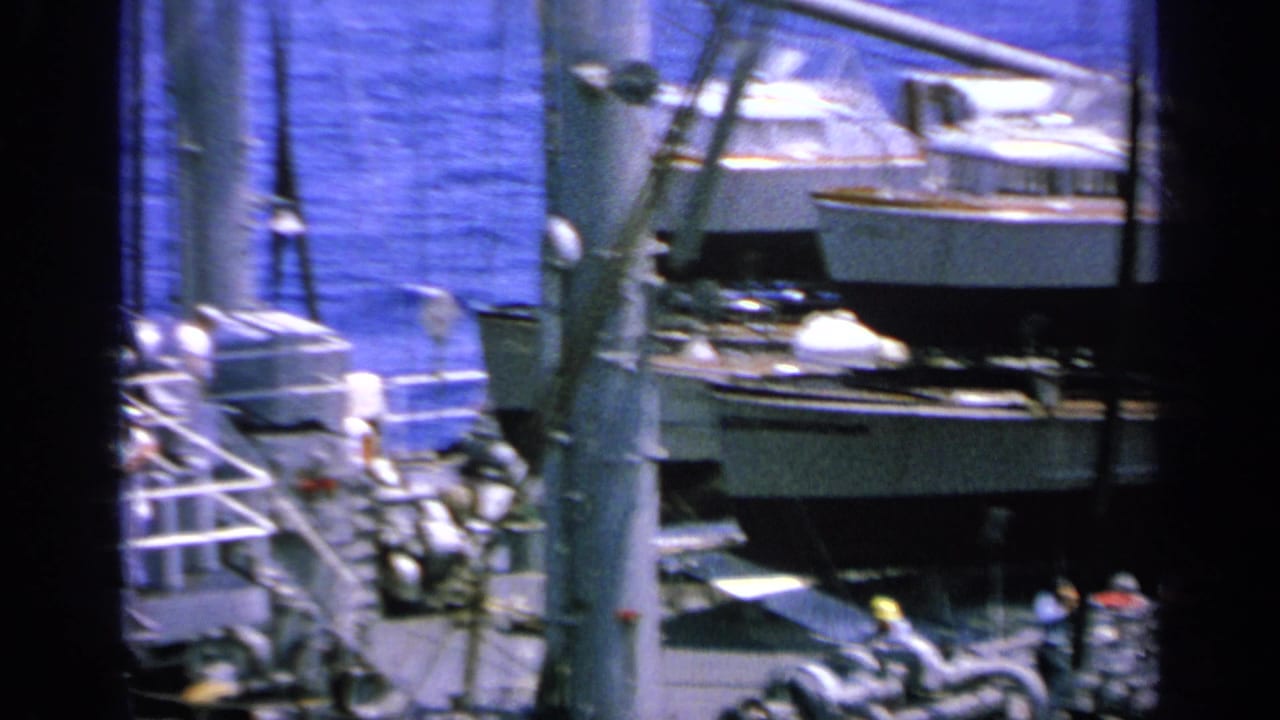 1963 Greece 8mm view across a ship deck, with a small boat or lifeboat, railings, rigging, and blue water in the background.