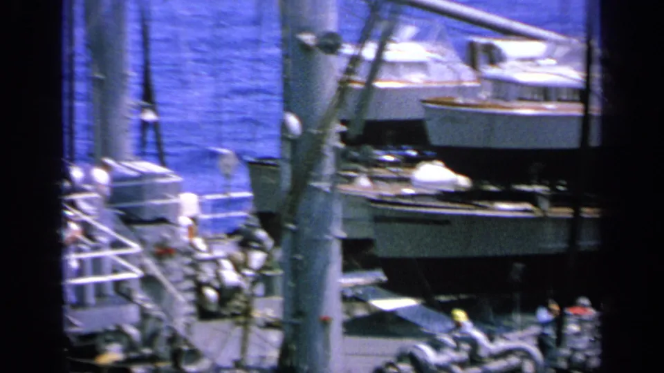 1963 Greece 8mm view across a ship deck, with a small boat or lifeboat, railings, rigging, and blue water in the background.