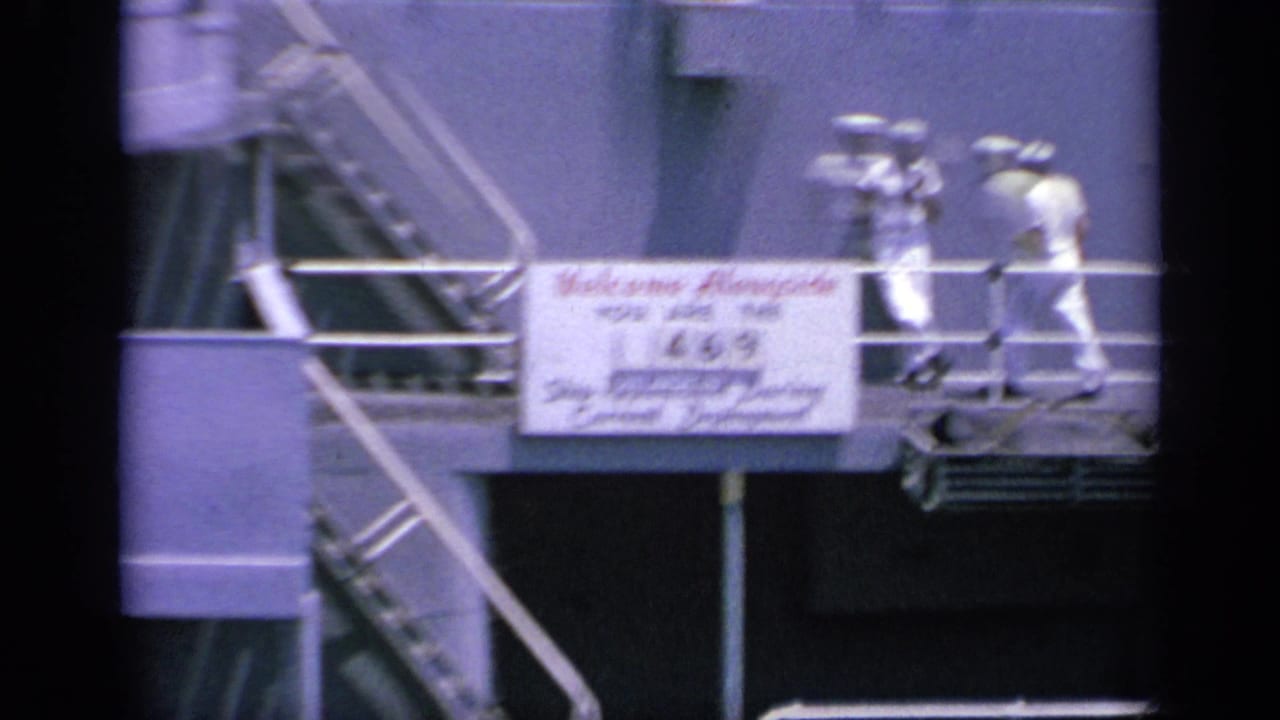 1963 Greece 8mm frame with two sailors moving along a metal gangway on a naval ship, beside a sign welcoming alongside replenishment.