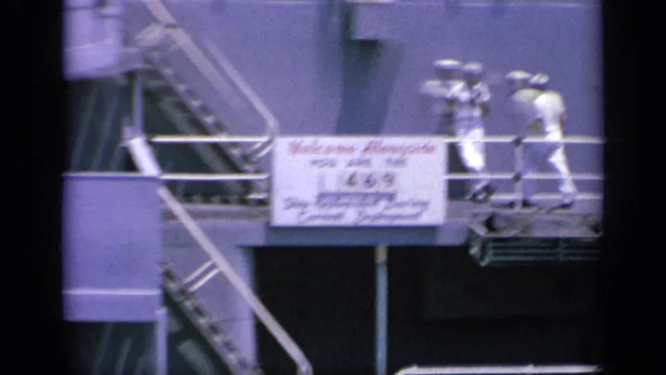 1963 Greece 8mm frame with two sailors moving along a metal gangway on a naval ship, beside a sign welcoming alongside replenishment.
