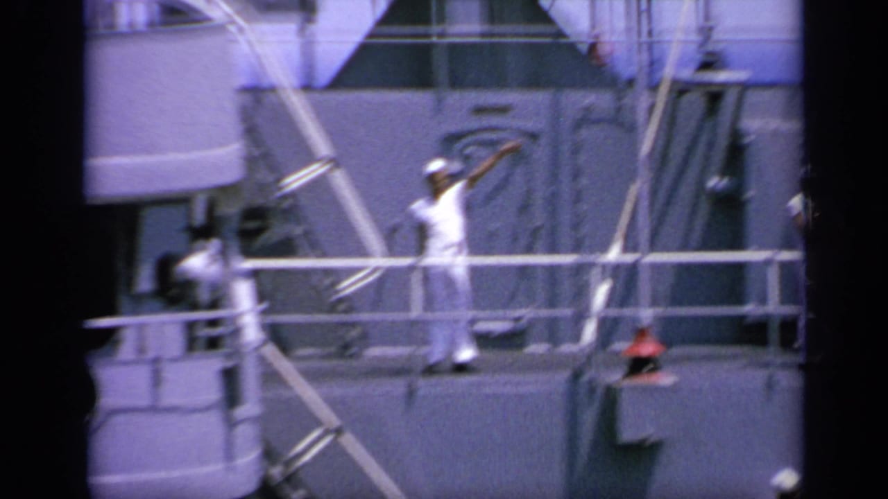 1963 Greece 8mm frame showing a sailor waving on a naval ship deck, with railings, rigging or cables, and another crew member nearby.