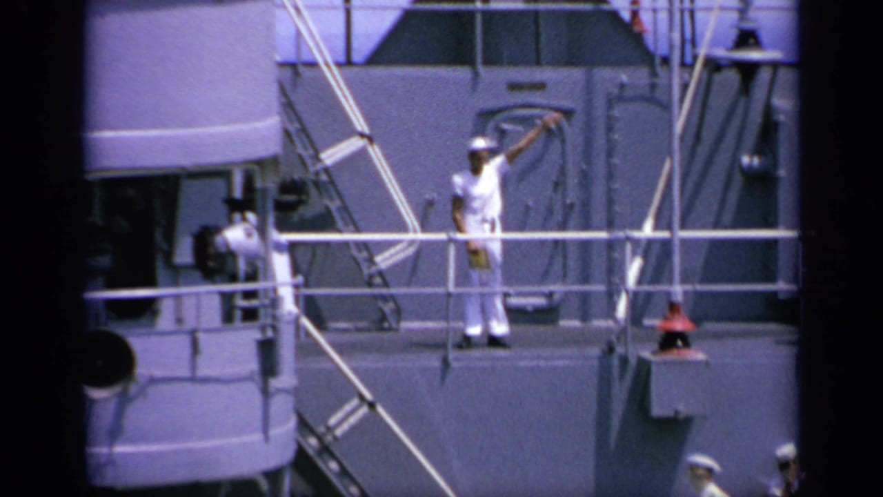 Sailor continues flag signaling beside railings and ship equipment.