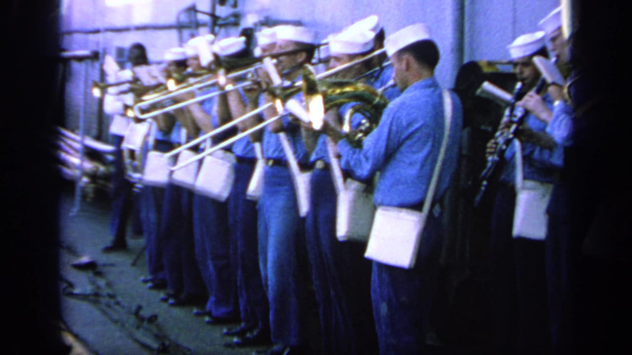 Close shipboard view of U.S. Navy band members in blue shirts and white caps playing brass instruments in 1963 Greece footage.