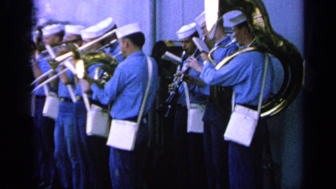 Shipboard Navy band performance with tuba, trombones, and clarinet-like woodwinds visible in faded 8mm color.