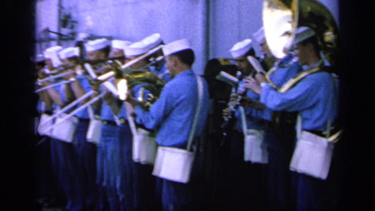 Sailors in blue and white uniforms play brass instruments on a ship deck.