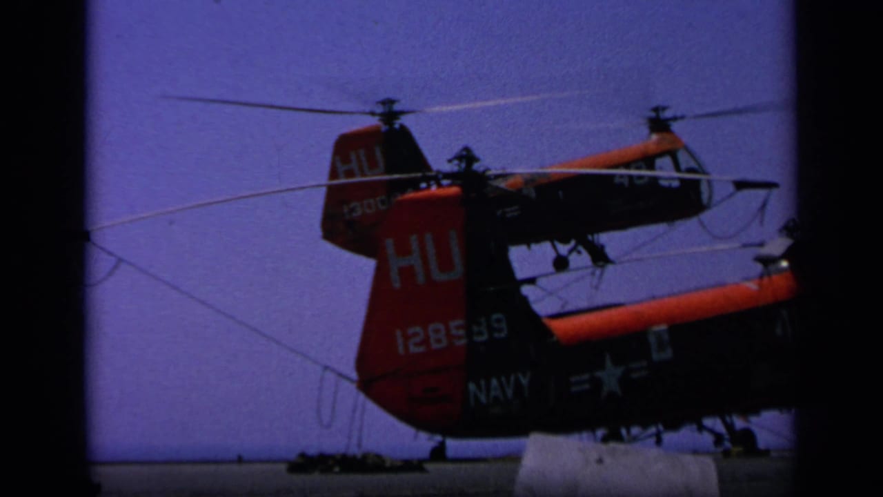 1963 Greece 8mm frame showing red and black Navy helicopters on a carrier deck, with tail markings and spinning rotors visible.