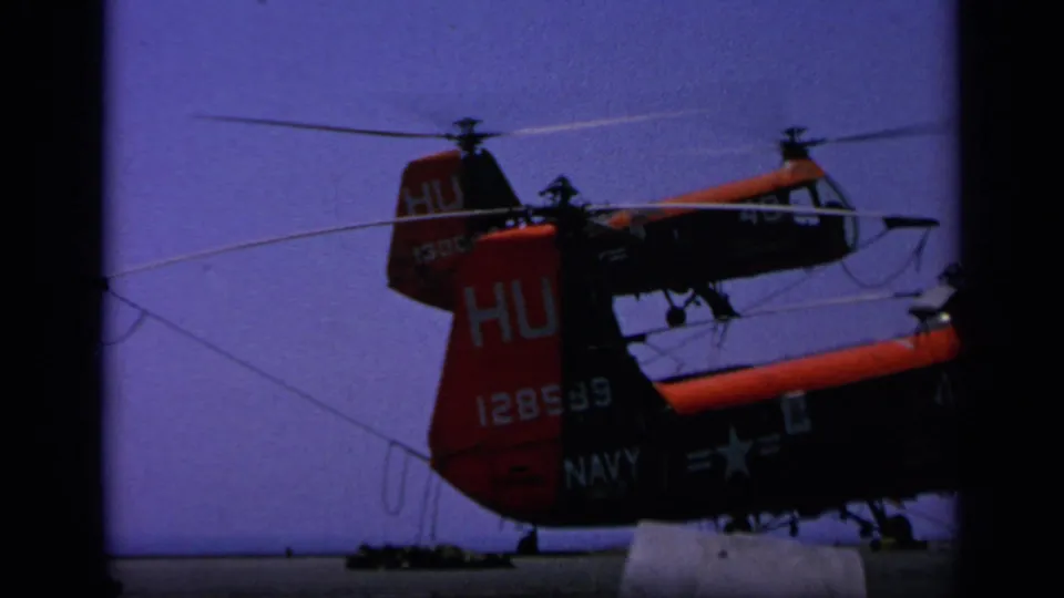 1963 Greece 8mm frame showing red and black Navy helicopters on a carrier deck, with tail markings and spinning rotors visible.