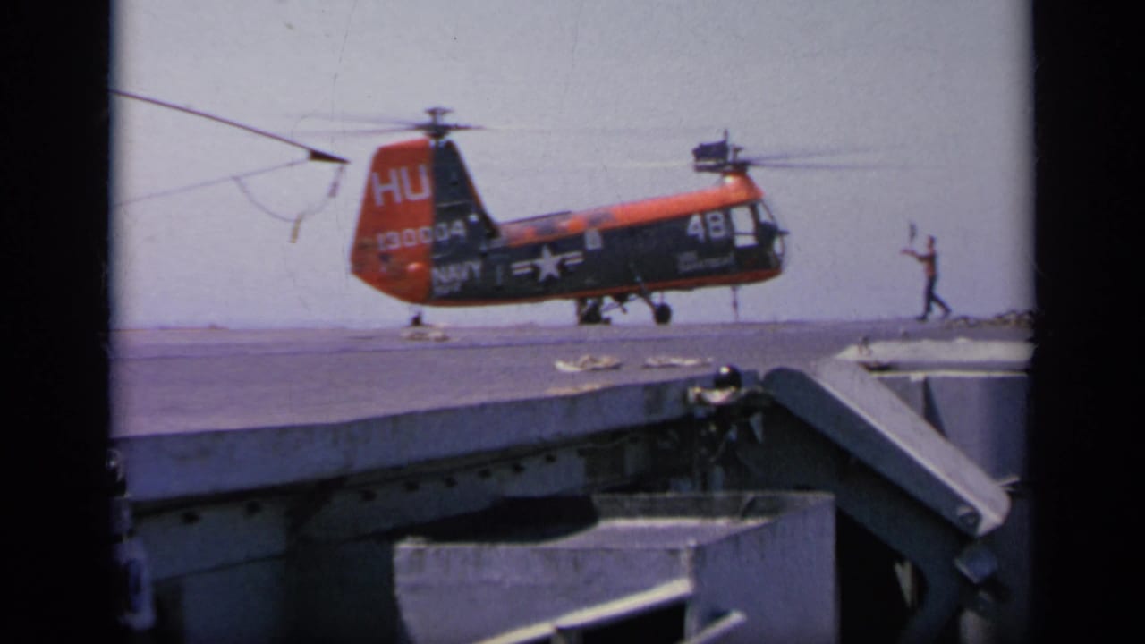 1963 Greece home-movie frame of a Navy helicopter marked 130004 and 48 approaching the deck while crew guide it in.