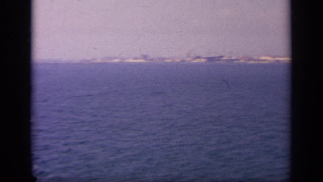 Distant shoreline and white buildings across blue water under a hazy sky.