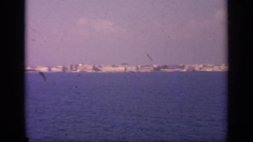 1963 Greece 8mm frame with blue sea in the foreground and a distant coastal town running across the horizon.